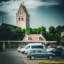 Voorgevel van winkel met rode bakstenen dak, kerkflat op achtergrond en geparkeerde auto's op het plein