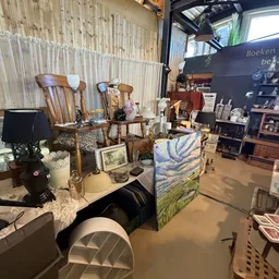 Binnenaanzicht van kringloopwinkel met houten meubels, kunstwerken, kunstnijverheidsspullen en diverse tweedehandsartikelen u