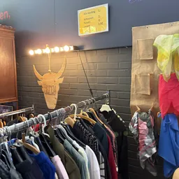 Rekken met tweedehands kleding onder verlichte spiegel met gouden stierenschedel decoratie