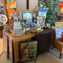 Houten tafel met gestapeld servies, keukengereedschap en decoratieve items in thrift store