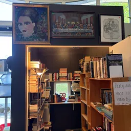 Interieur van een boekwinkel met houten boekenkasten, lamp en kunstwerken aan de muur