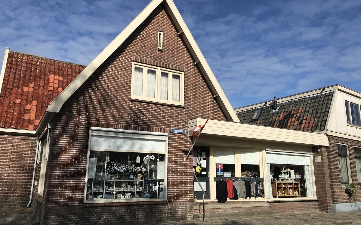 Voorgevel van een bakstenen kringloopwinkel met twee uitstalkassen en gevel met spits dak