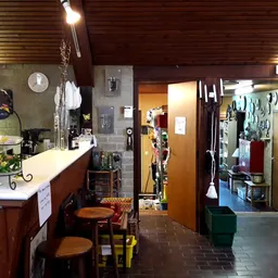 Binnenaanzicht kringloopwinkel met toonbank links, diverse stellingen en winkelrekken, houten plafond en bruine tegelvloer