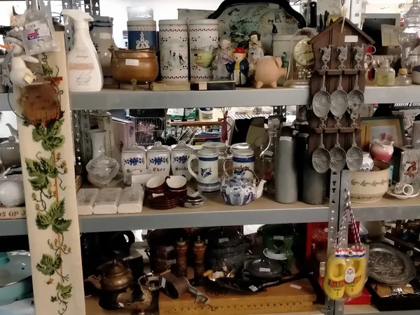 Stellingen vol huishoudelijke spullen, servies, kopjes, kannen en decoratieve items in een kringloopwinkel