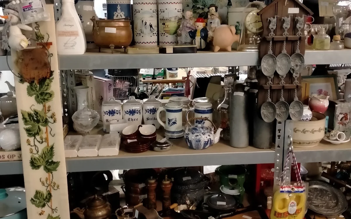 Stellingen vol huishoudelijke spullen, servies, kopjes, kannen en decoratieve items in een kringloopwinkel