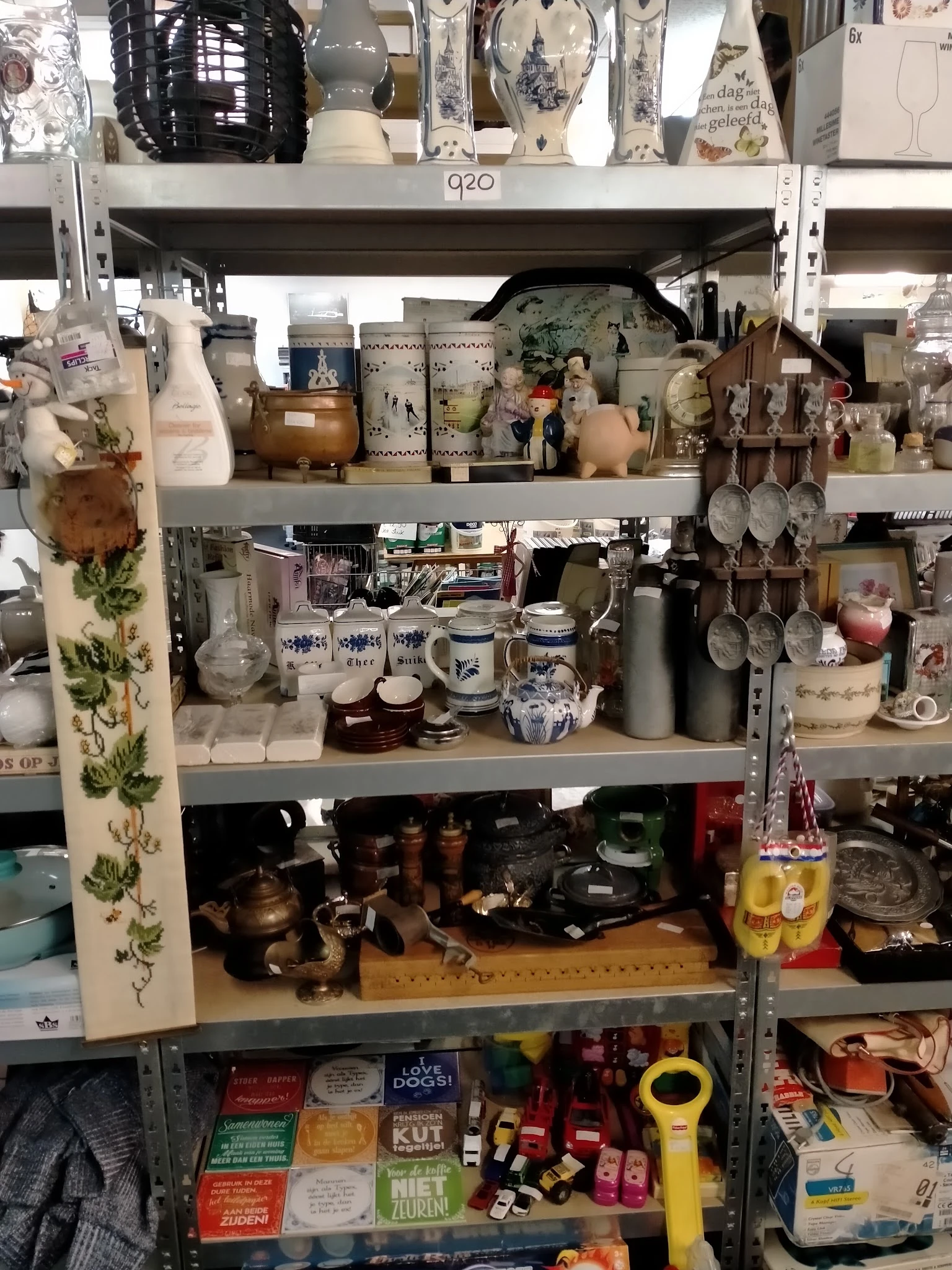 Stellingen vol huishoudelijke spullen, servies, kopjes, kannen en decoratieve items in een kringloopwinkel