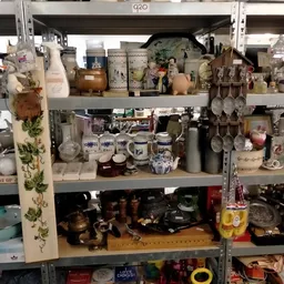 Stellingen vol huishoudelijke spullen, servies, kopjes, kannen en decoratieve items in een kringloopwinkel