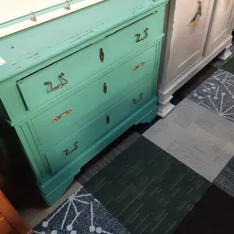 Turquoise commode met vier laden en koperen handles, zijkant gefotografeerd