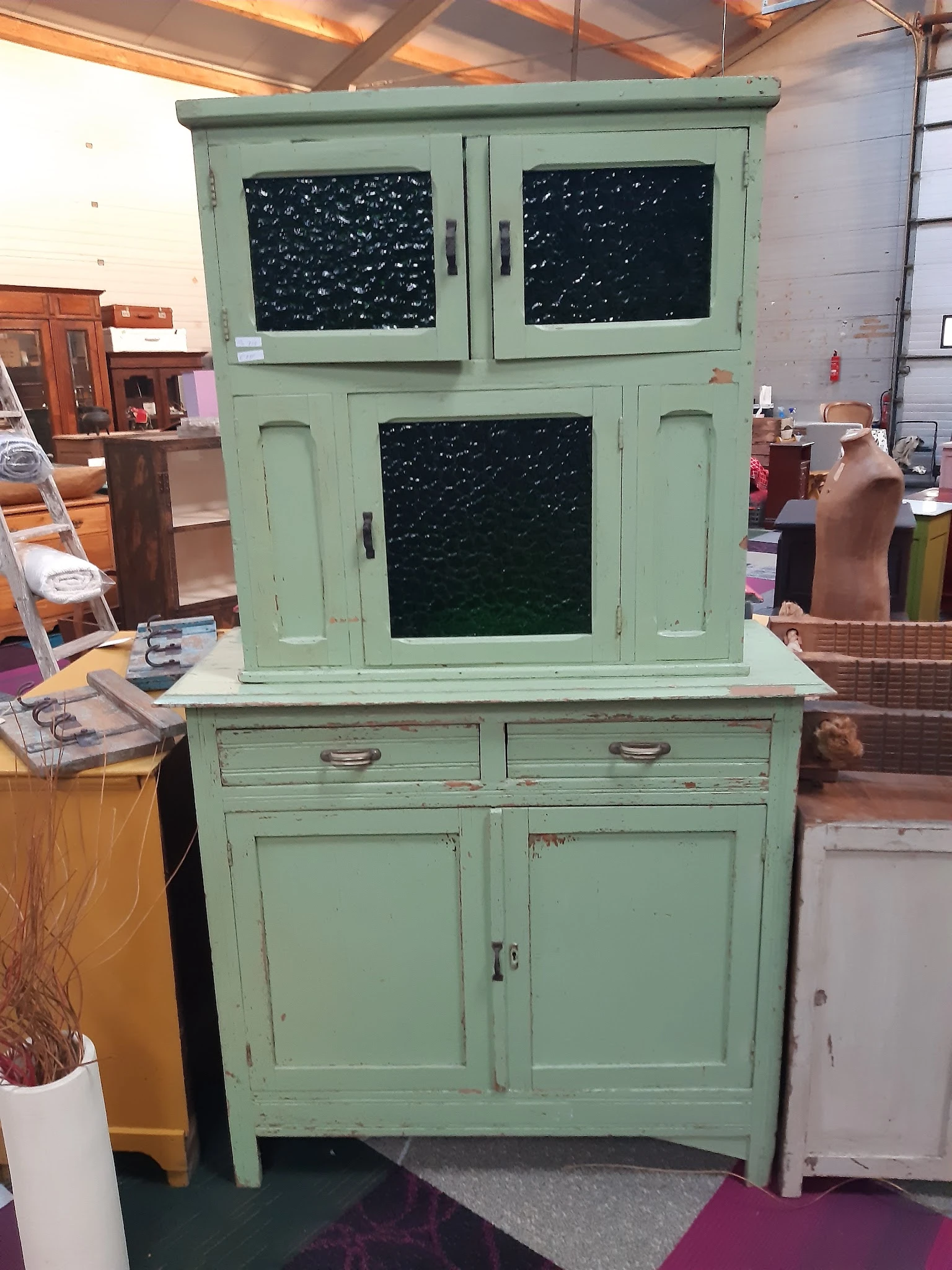 Groen geschilderd vintage kastje met glazen deuren bovenin en twee lades en kastdeuren onderin