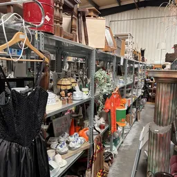 Lange rijen metalen stellingen met huishoudartikelen, servies, lampen en decoratie in een kringloopwinkel