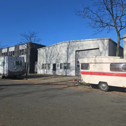 Grijze en witte bedrijfsgebouwen met nummer 30 aan de voorgevel, enkele caravans op het parkeerterrein