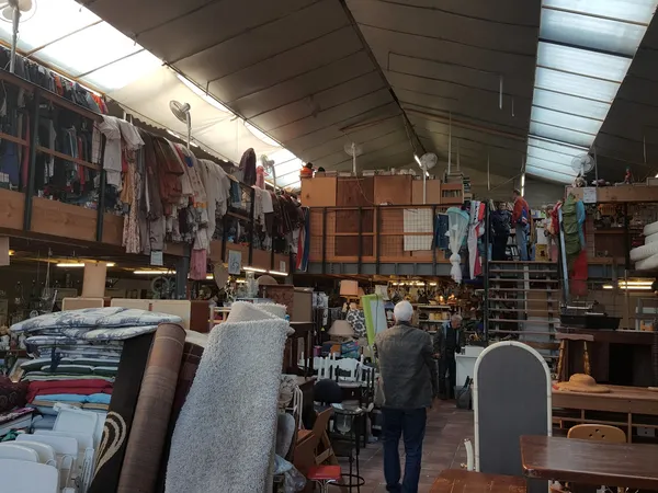 Ruim interieur van kringloopwinkel met kledingrekken, meubels en diverse goederen langs de wanden en stellingen