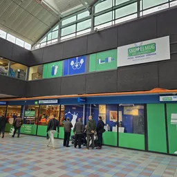 Winkelinterieur met blauwe en groene gevels, stellingen met spullen en bezoekers in de kringloopwinkel