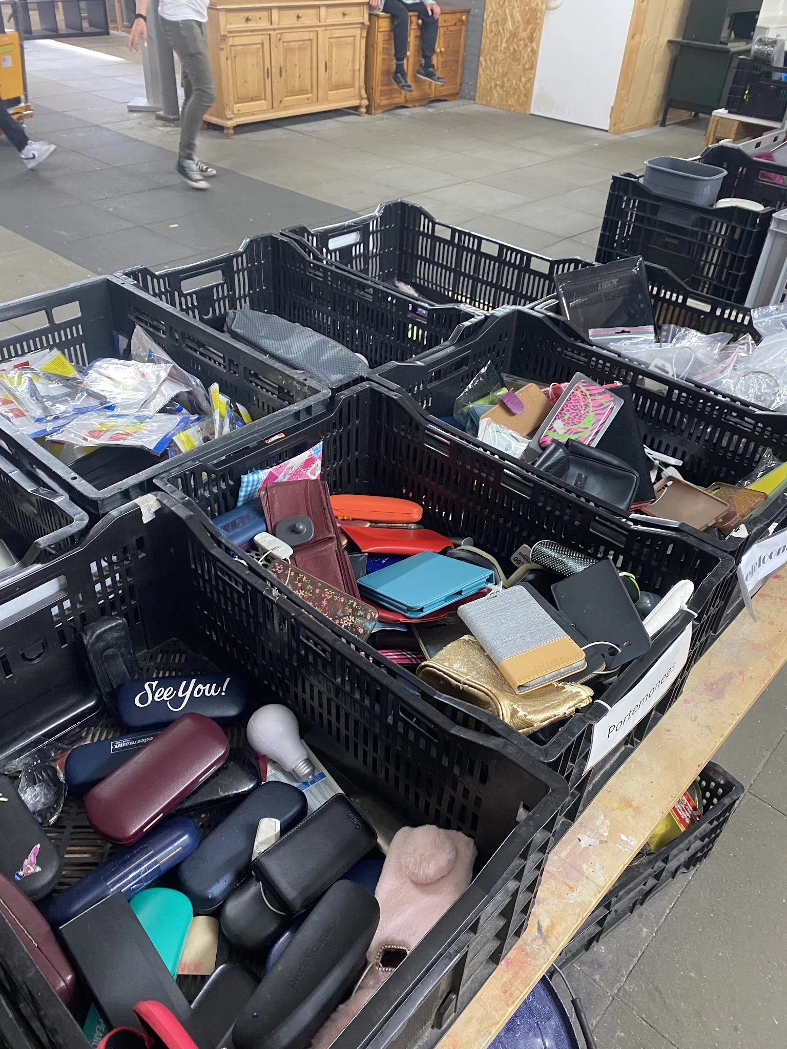 Zwarte kunststof kratten vol met tweedehands portemonnees, tasjes en accessoires in verschillende kleuren