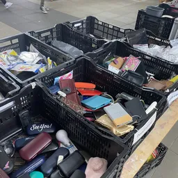 Zwarte kunststof kratten vol met tweedehands portemonnees, tasjes en accessoires in verschillende kleuren