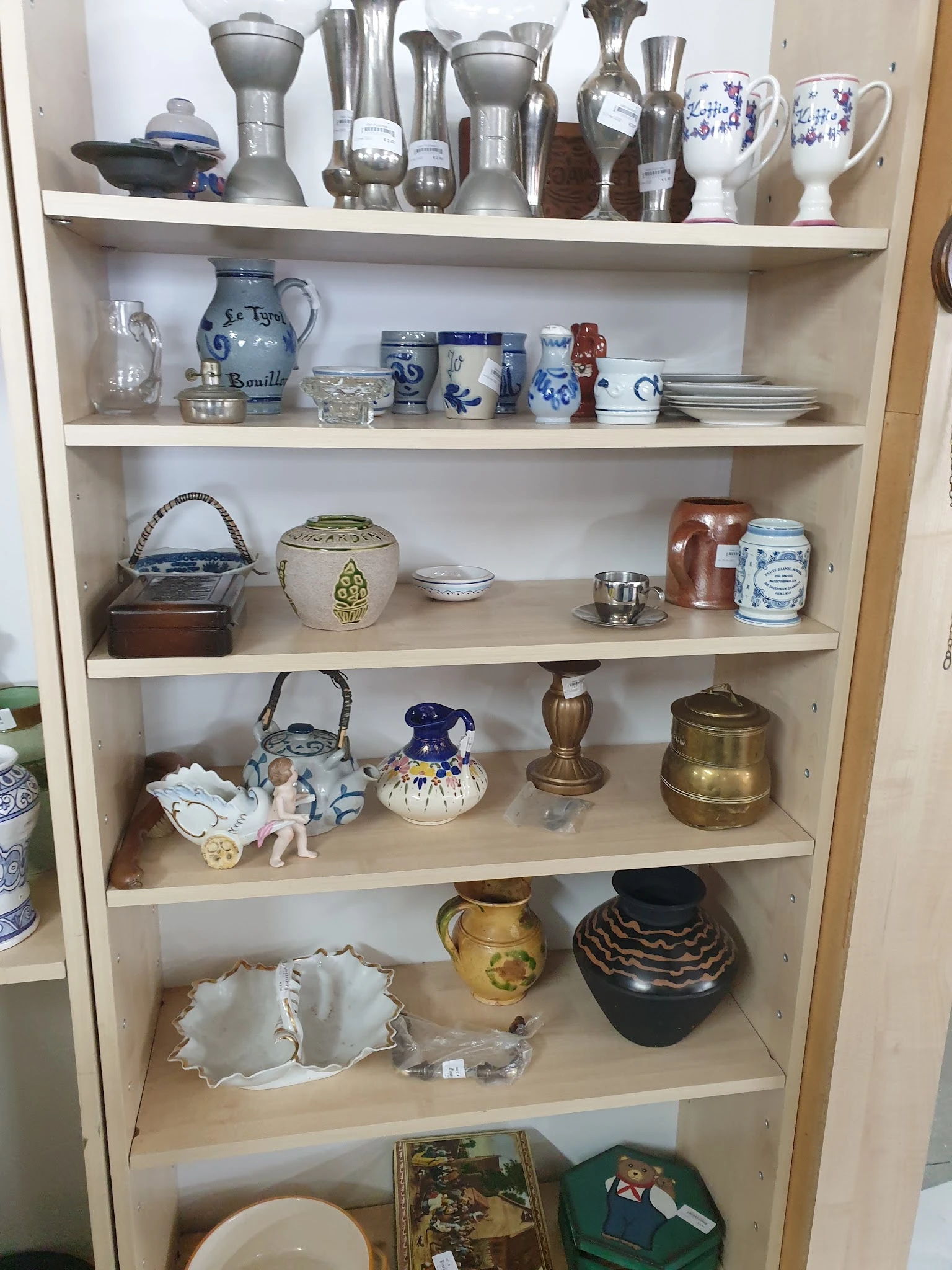 Glazen vitrinekast met decoratieve voorwerpen: blauw wit porselein, koperen items, vazen en diverse verzamelelementen