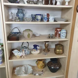 Glazen vitrinekast met decoratieve voorwerpen: blauw wit porselein, koperen items, vazen en diverse verzamelelementen