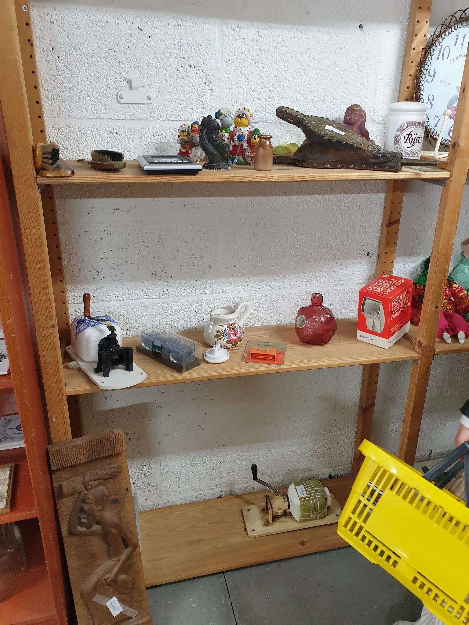 Houten stellingkast met diverse tweedehands spullen zoals een theepot, rode decoratieve objecten en ander huishoudelijk goed