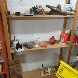 Houten stellingkast met diverse tweedehands spullen zoals een theepot, rode decoratieve objecten en ander huishoudelijk goed