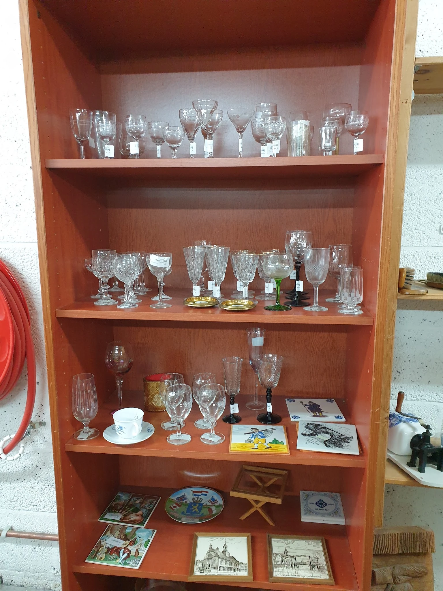 Glazenkast met diverse glazen en serviesgoed, waaronder wijnglazen, drinkglazen en kopjes op verschillende planken