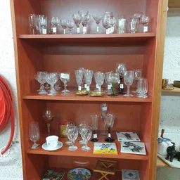 Glazenkast met diverse glazen en serviesgoed, waaronder wijnglazen, drinkglazen en kopjes op verschillende planken