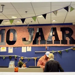 Interieur van kringloopwinkel met groot banner '10 JAAR', klant aan balie, decoratieve vlaggetjes
