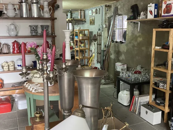 Binnenaanzicht van kringloopwinkel met stellingen, keukengerei, kandelaars en diverse spullen