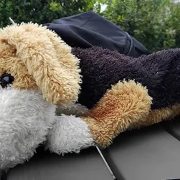 Drie pluchen speelgoedbeesten in verschillende kleuren liggend op elkaar op een grijze ondergrond