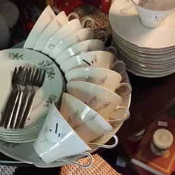 Servies met decoratieve motieven: stapel kopjes met oren, schotels en vorken op een donkere ondergrond