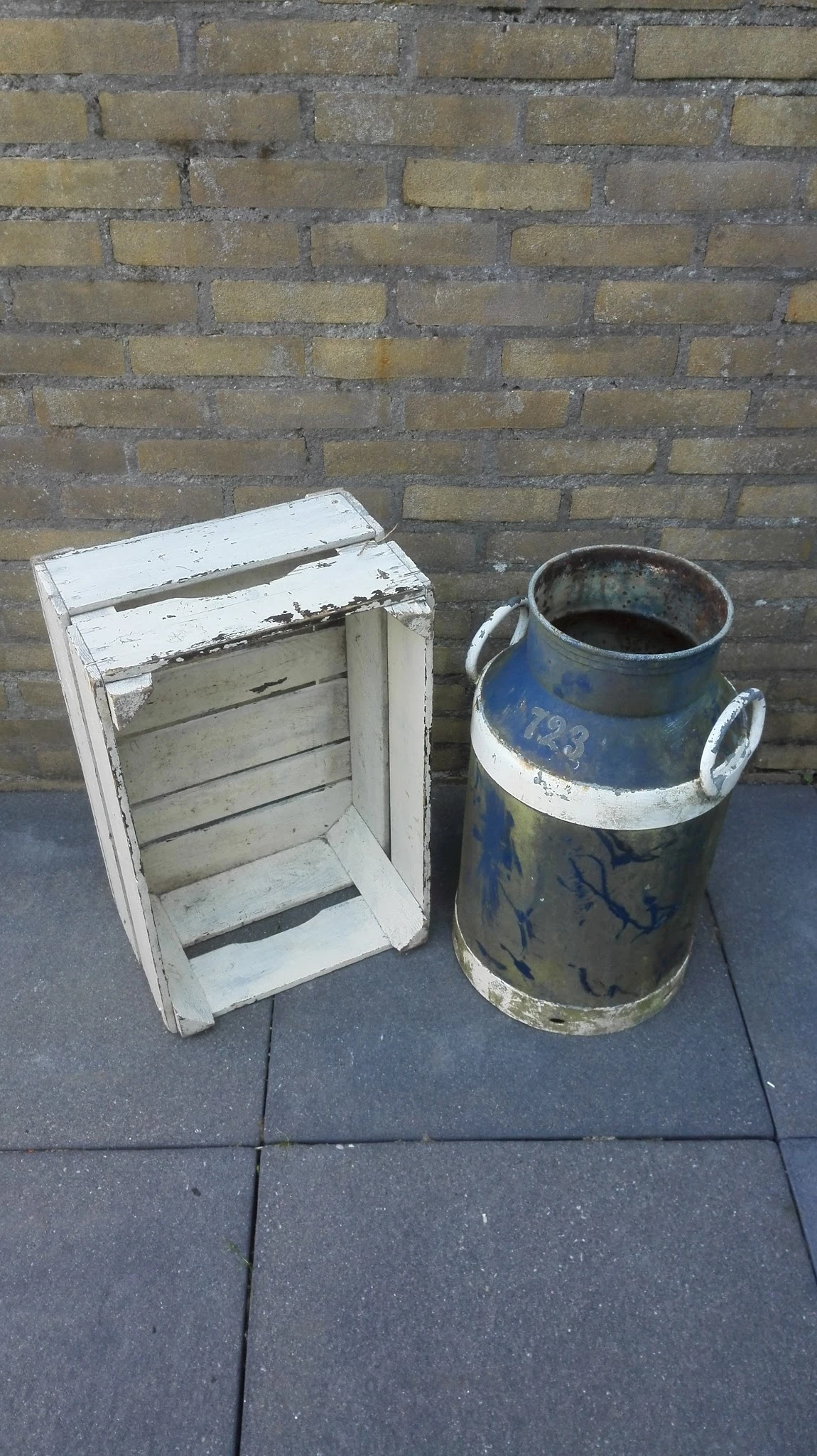 Witte houten krat en blauwe melkkan met metalen hengsels op betonnen ondergrond