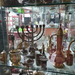 Vitrinekast met antieke en vintage items: kandelaar, koperen vazen, theepotten en decoratieve objecten