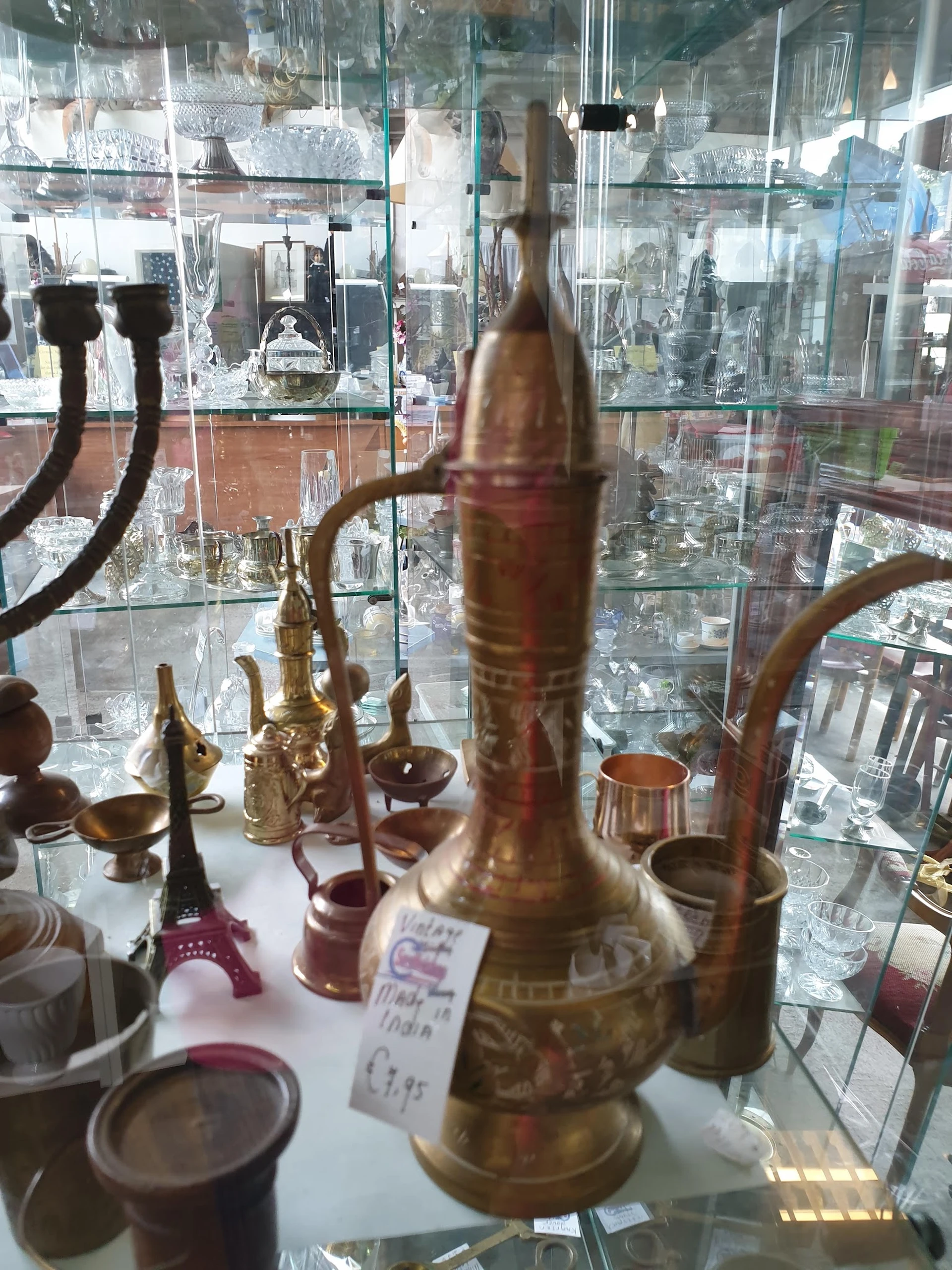 Verzameling van koperen en bronzen decoratieve items waaronder kandelaars en vazen, uitgestald op een plank met uitzicht op d