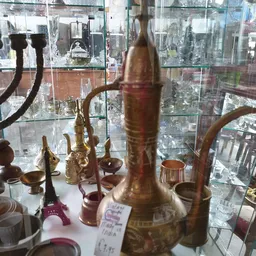 Verzameling van koperen en bronzen decoratieve items waaronder kandelaars en vazen, uitgestald op een plank met uitzicht op d