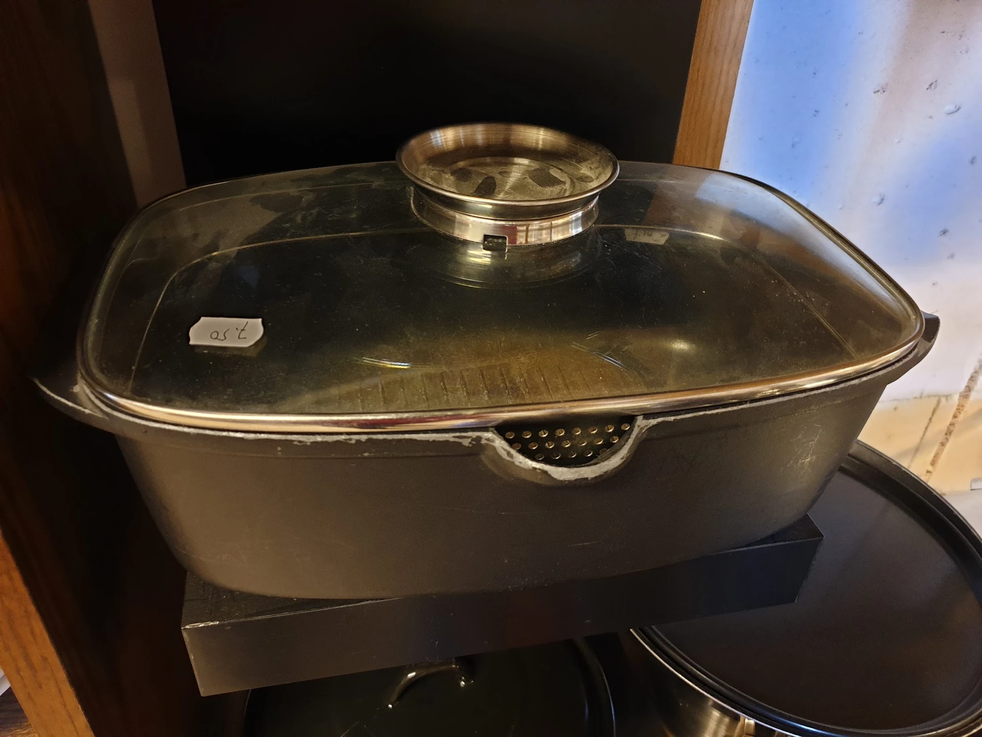 Zwarte braadpan met glasdeksel en gouden handvat op zwart oppervlak