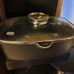 Zwarte braadpan met glasdeksel en gouden handvat op zwart oppervlak