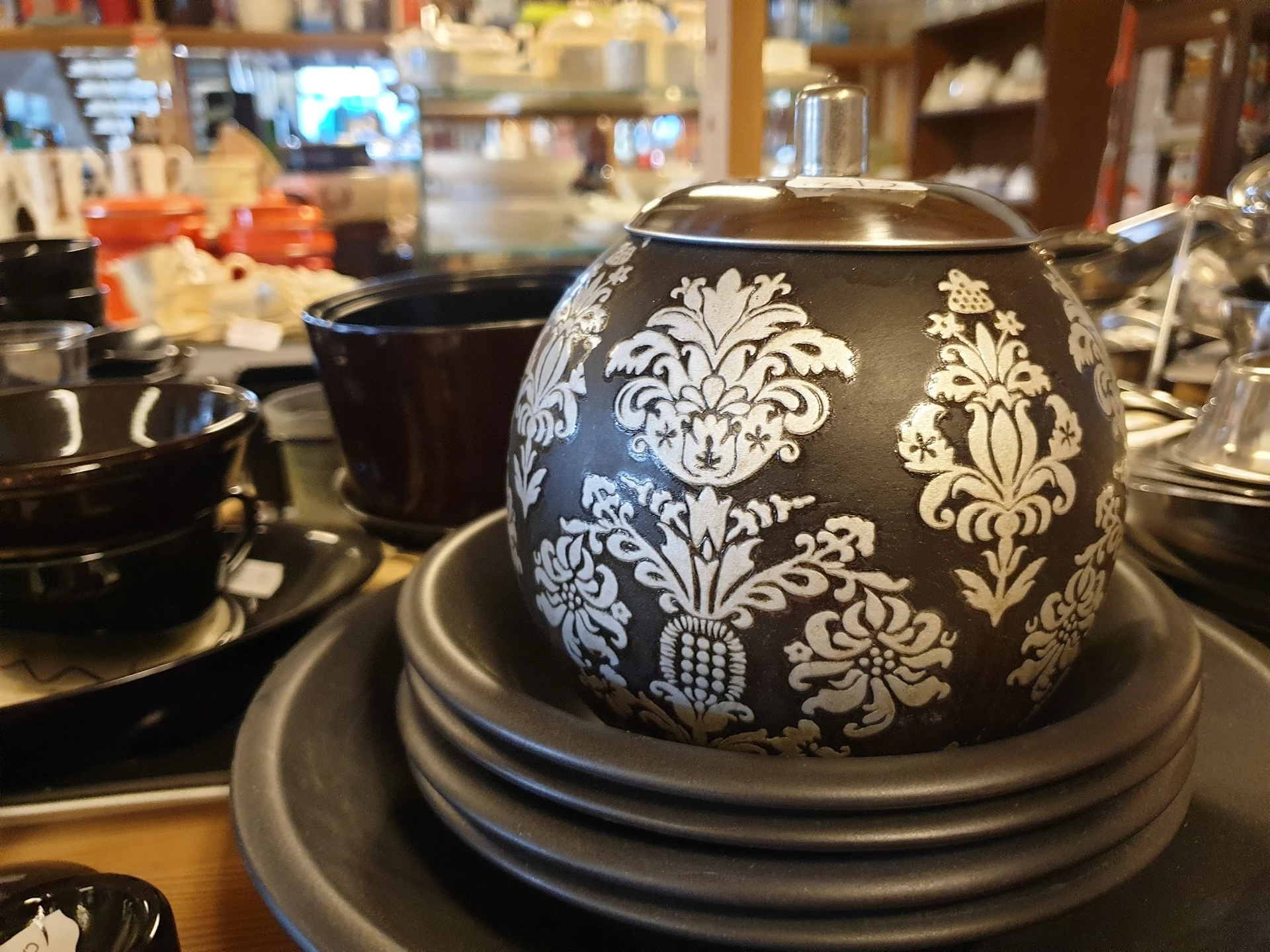 Zwarte theepot met wit damastpatroon op grijze onderzetter, tussen ander servies op tafel