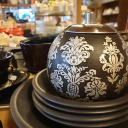 Zwarte theepot met wit damastpatroon op grijze onderzetter, tussen ander servies op tafel