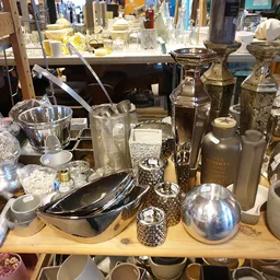 Tafel vol tweedehands serviesgoed, glazen en metalen huishoudartikelen in diverse stijlen