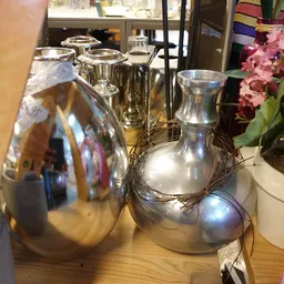 Glazen vazen en kandelaars, waaronder zilveren en transparante exemplaren, op een tafel naast roze bloemen