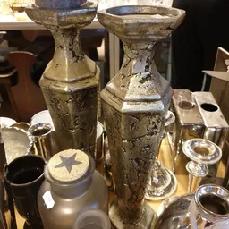 Twee antieke glazen flessen met goudkleurige patina en decoratieve details, omgeven door ander kristal- en glaswerk op een di
