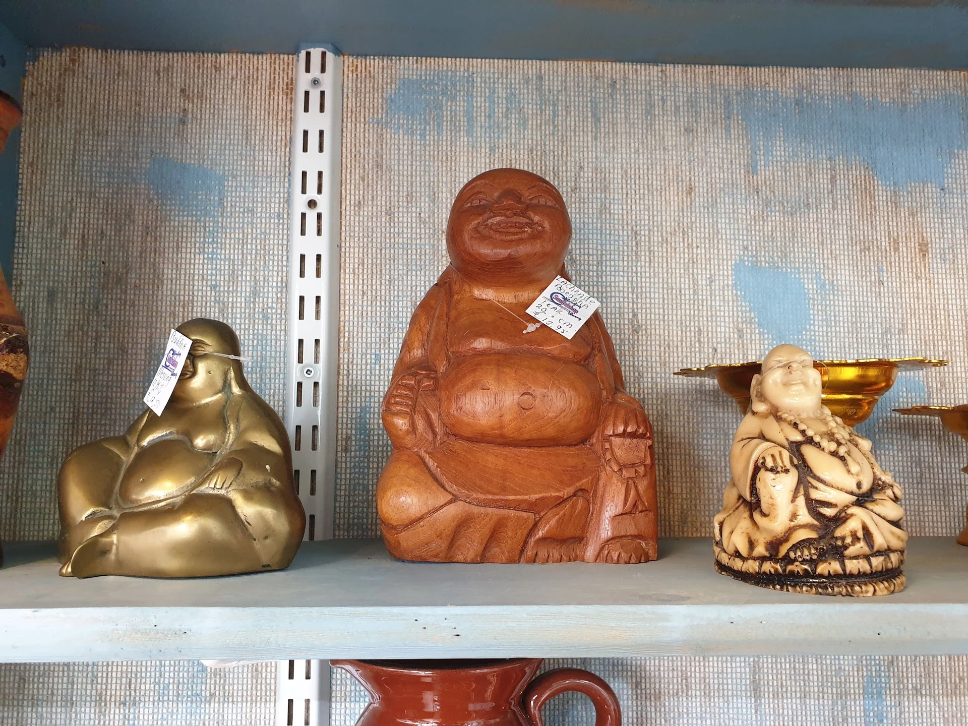 Drie decoratieve boeddhabeelden in verschillende materialen en kleuren op een plank