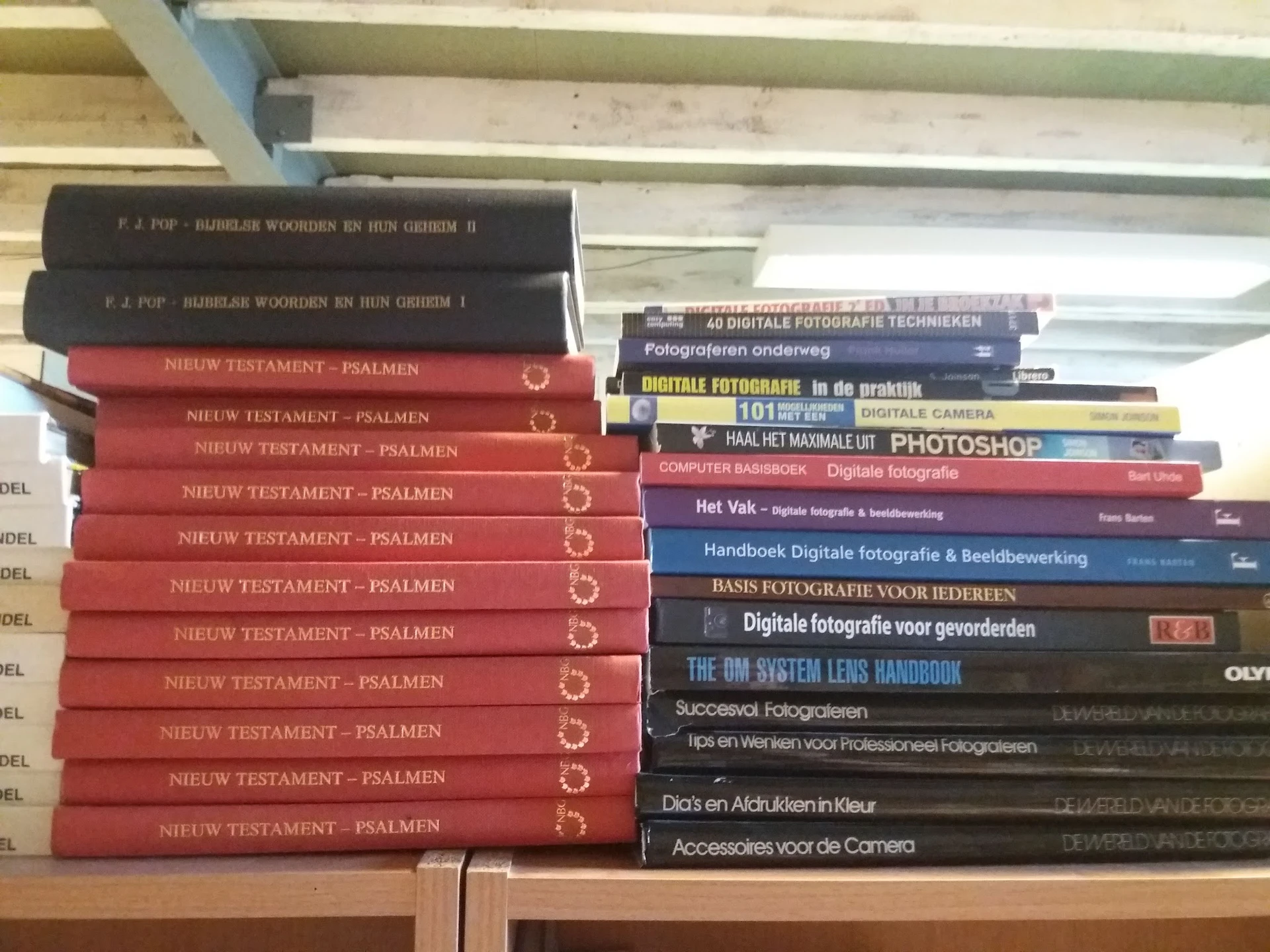 Boekenrekken met tweedehands boeken, waaronder meerdere exemplaren van 'Nieuw Testament - Psalmen' en fotografie-handboeken