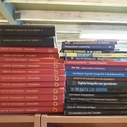 Boekenrekken met tweedehands boeken, waaronder meerdere exemplaren van 'Nieuw Testament - Psalmen' en fotografie-handboeken