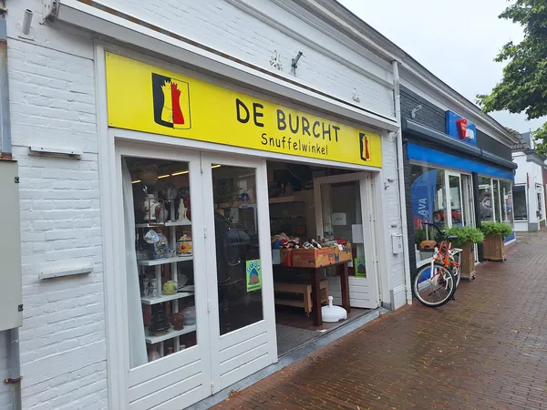 Gevel van kringloopwinkel De Burcht met geel logo, witte houten winkelpui en etalages met spullen