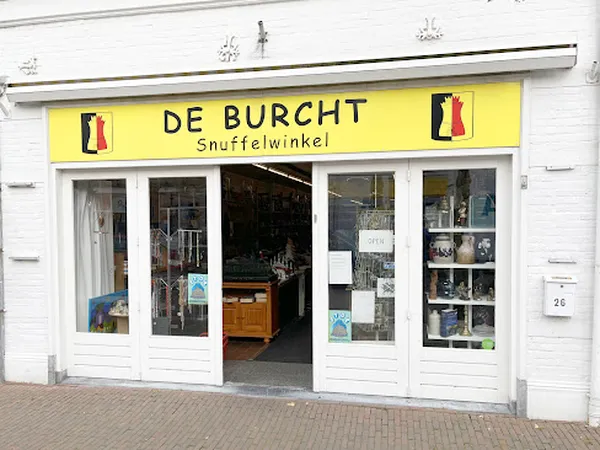 Gevel van kringloopwinkel De Burcht met gele luifel en witte raampartijen, winkelname leesbaar