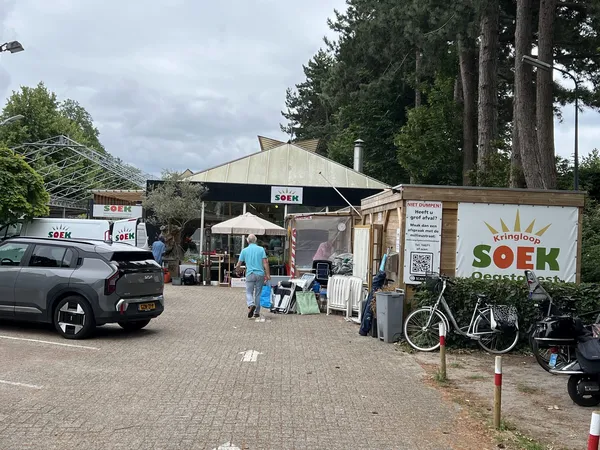 Voorkant van kringloopwinkel met parkeerplaats, fietsen en terras met parasol