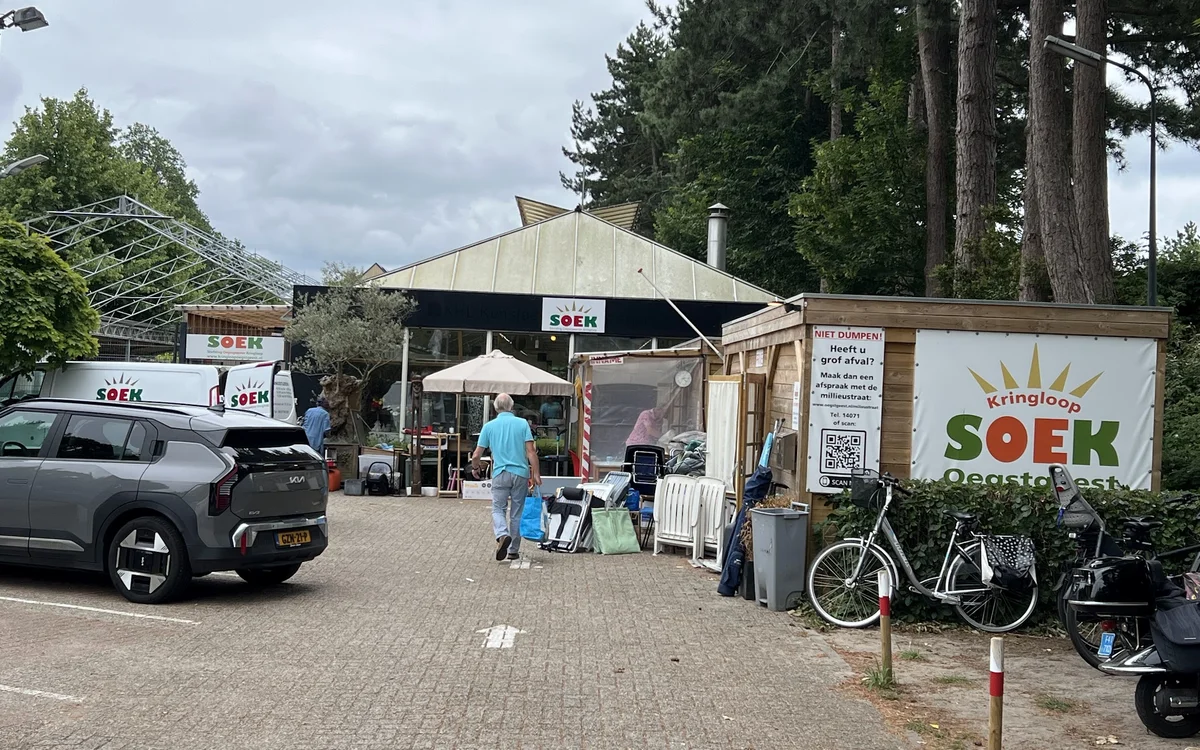 Voorkant van kringloopwinkel met parkeerplaats, fietsen en terras met parasol