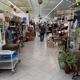 Winkelinterieur met diverse stellingen, meubels en spullen langs beide zijden van een gangpad met betonnen vloer