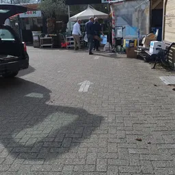 Straatscène met geparkeerde auto's, stellingen en spullen buiten voor een winkel
