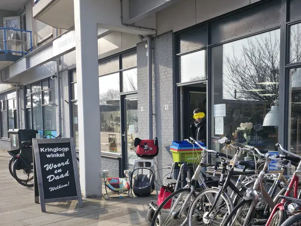 Voorgevel van kringloopwinkel met grote ramen, zwarte deur en fietsen geparkeerd ervoor
